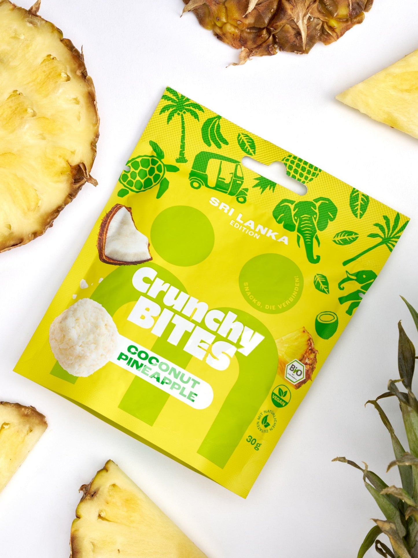myBuddy Crunchy Nut Bites Coconut Pineapple aus dem 9er-Set, einzelner 30-g-Beutel im Flatlay mit frischer Ananas und Kokosnuss