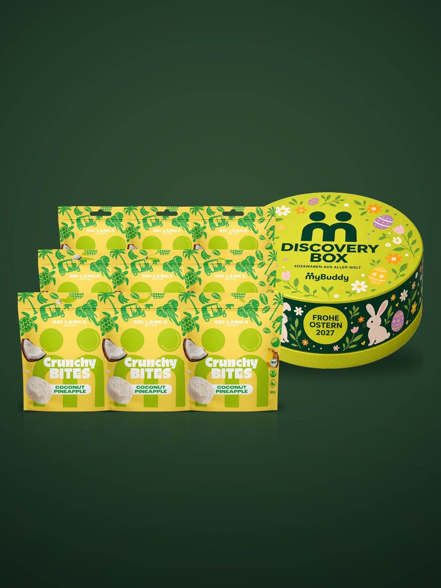 myBuddy HAVE IT ALL Starterpaket, Stimmungsbild: Discovery Box Ostern Edition und neun Beutel Crunchy Nut Bites Coconut Pineapple im Lichtkegel auf dunkelgrünem Grund
